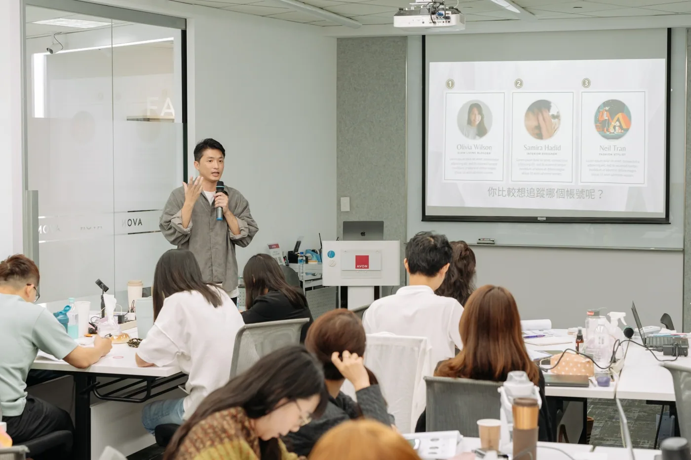 韓森在企業會議室裡拿著麥克風授課，學員圍著長桌做筆記